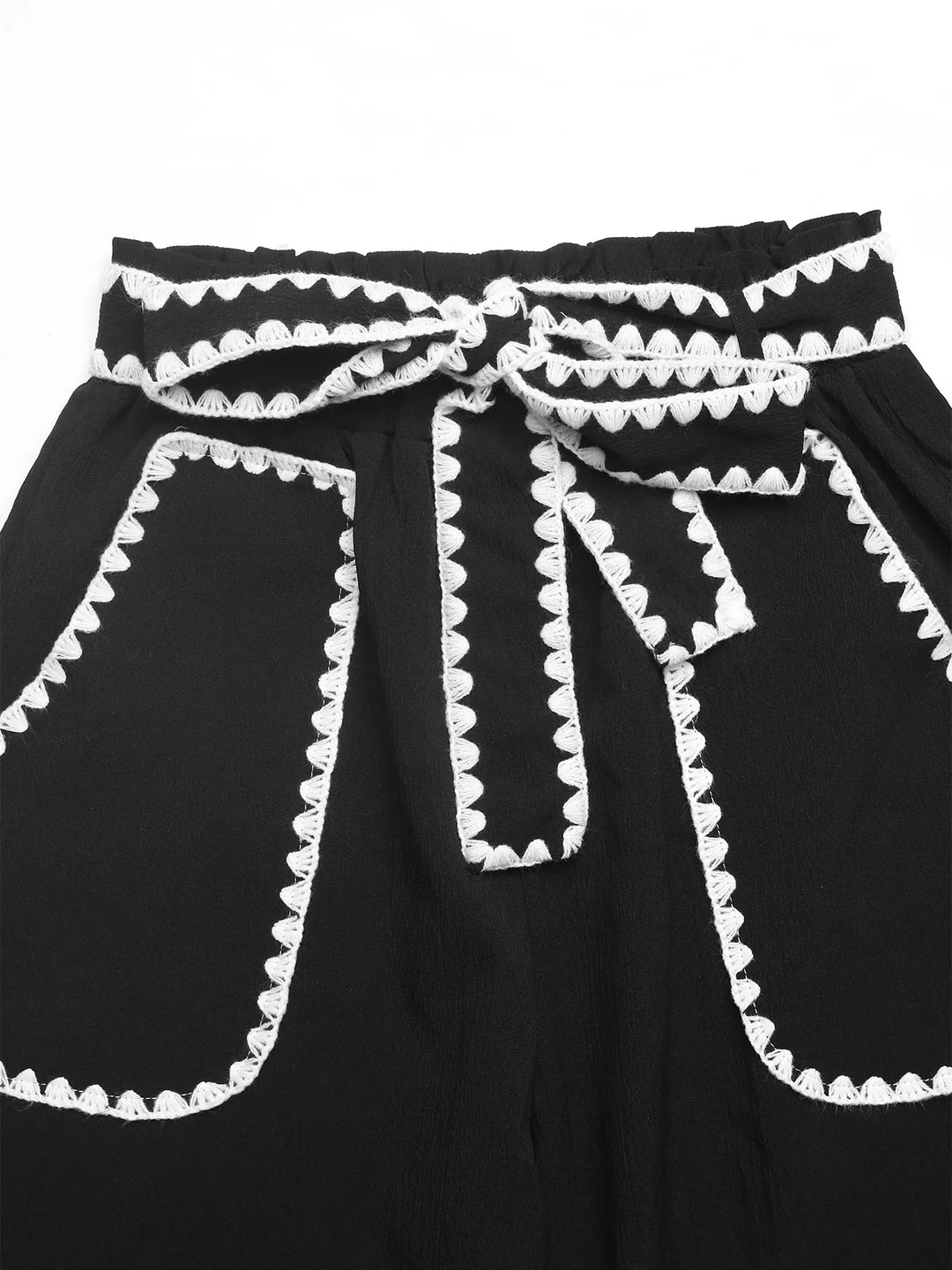 Close-up of the tie waist and scalloped trim pockets on black pants