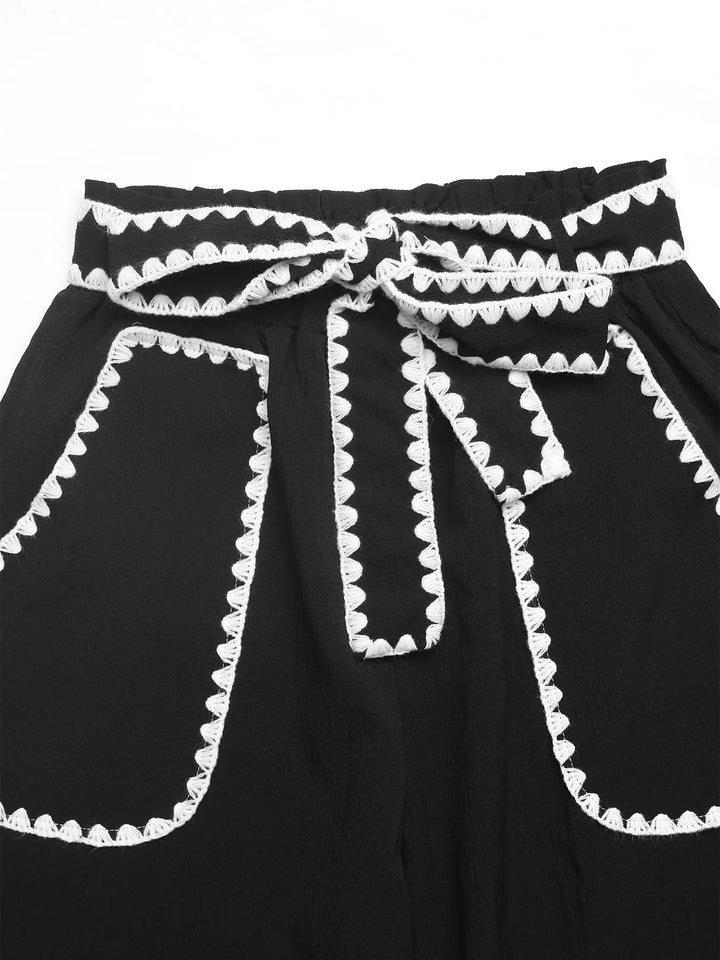 Close-up of the tie waist and scalloped trim pockets on black pants