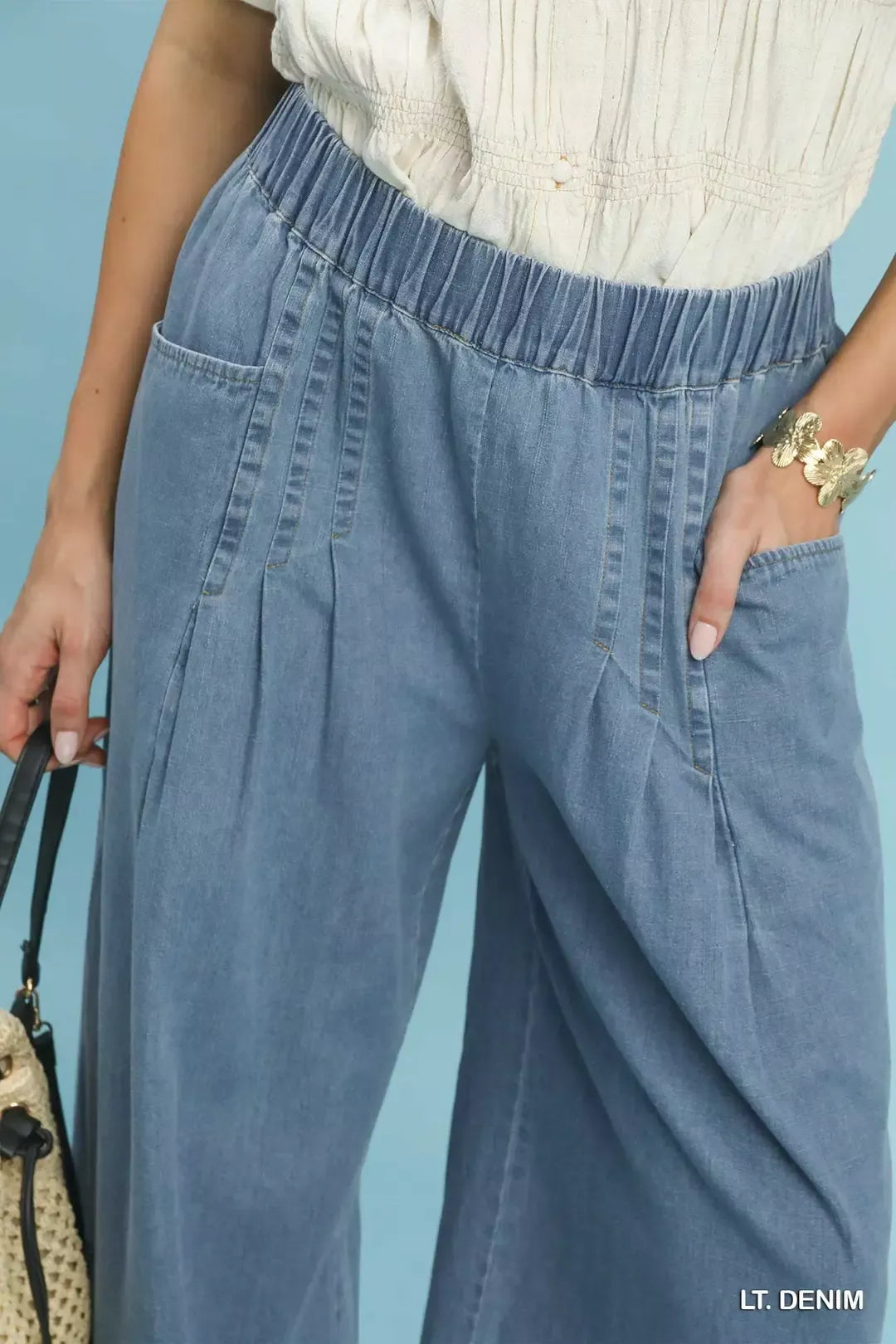 Close-up of the elastic waistband, pleats and side pocket on the light denim pants