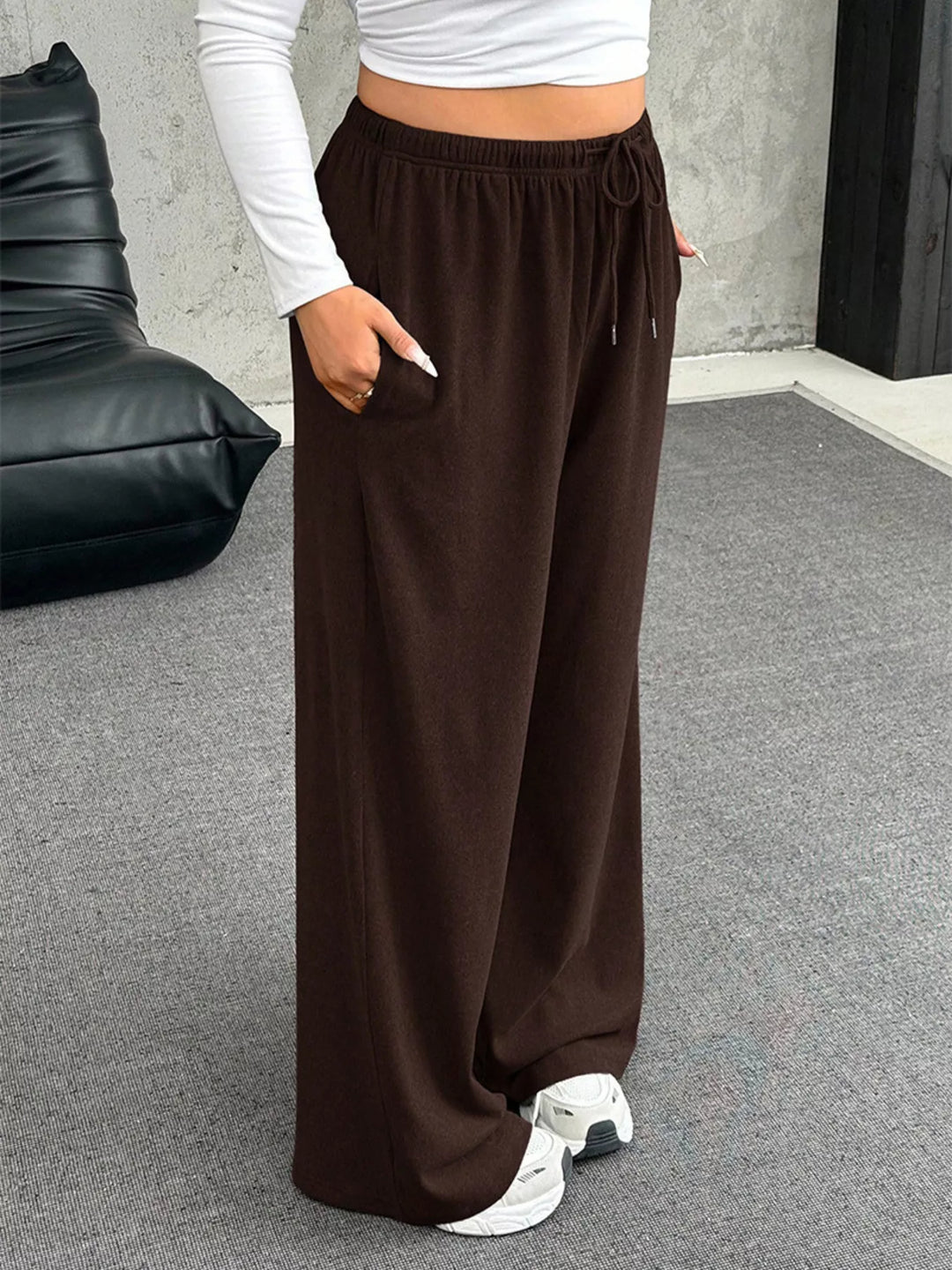 Brown wide leg pants with hand in pocket, angled view with white sneakers
