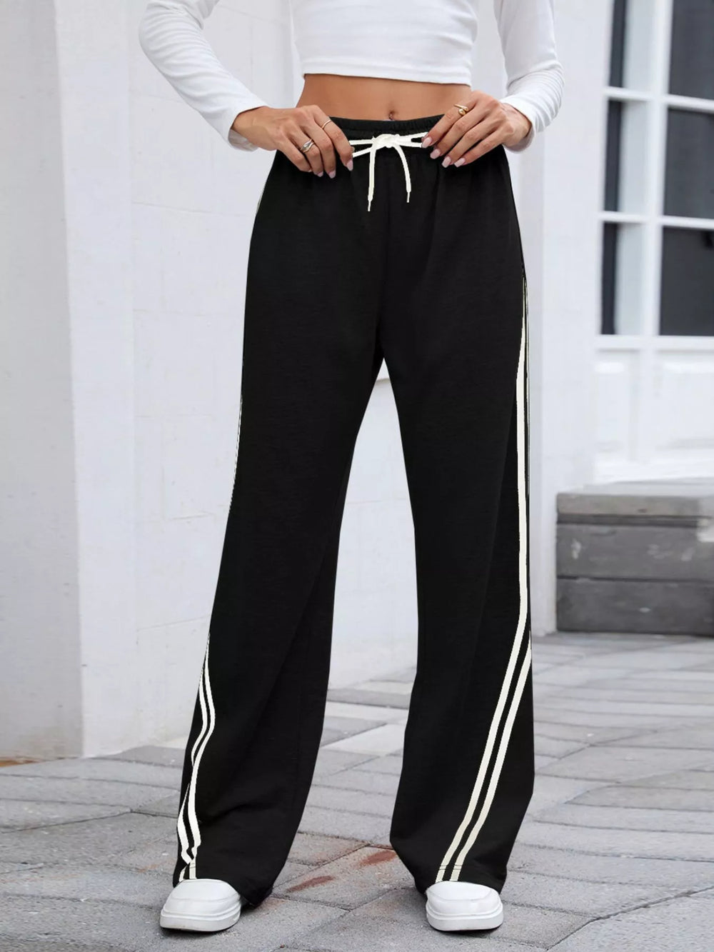 Black high rise drawstring pants with white side stripes, straight on front view