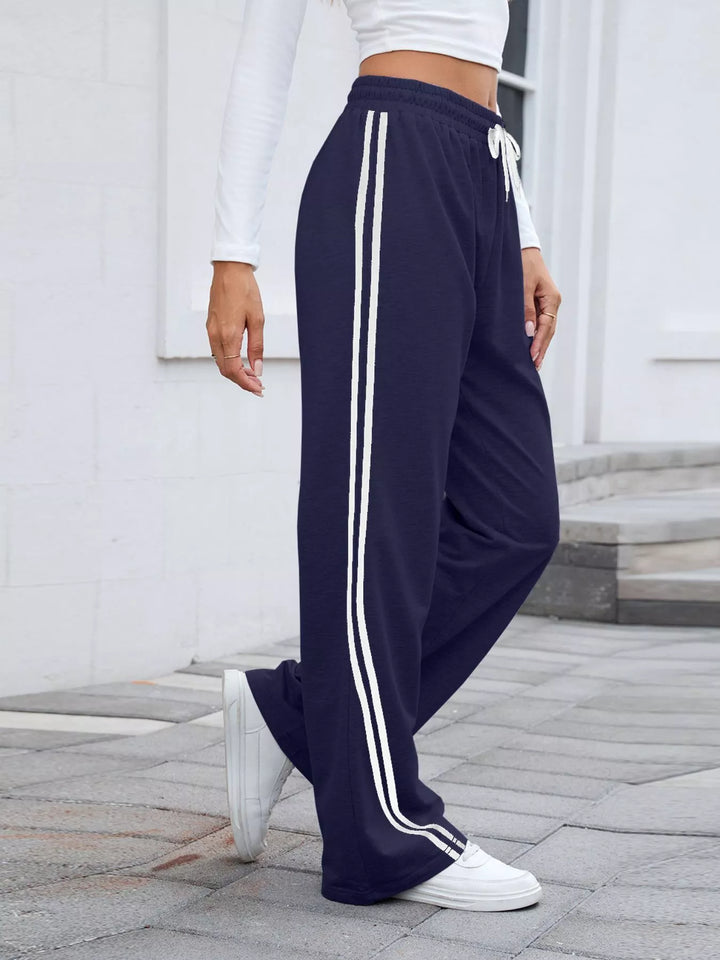 Navy wide leg pants with white side stripes, side view walking