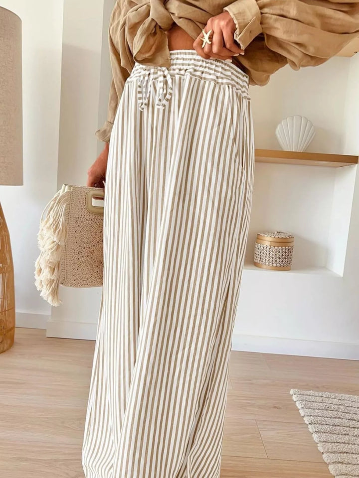 Front view of beige thin stripe flowy pants with a woven bag