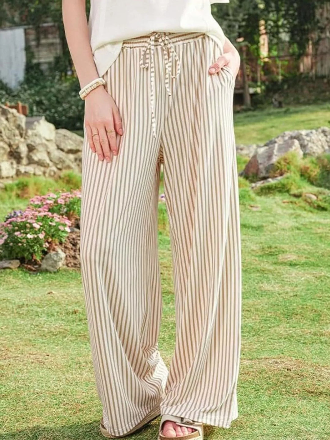 Beige striped wide leg pants with drawstring waist, hand in pocket on the lawn