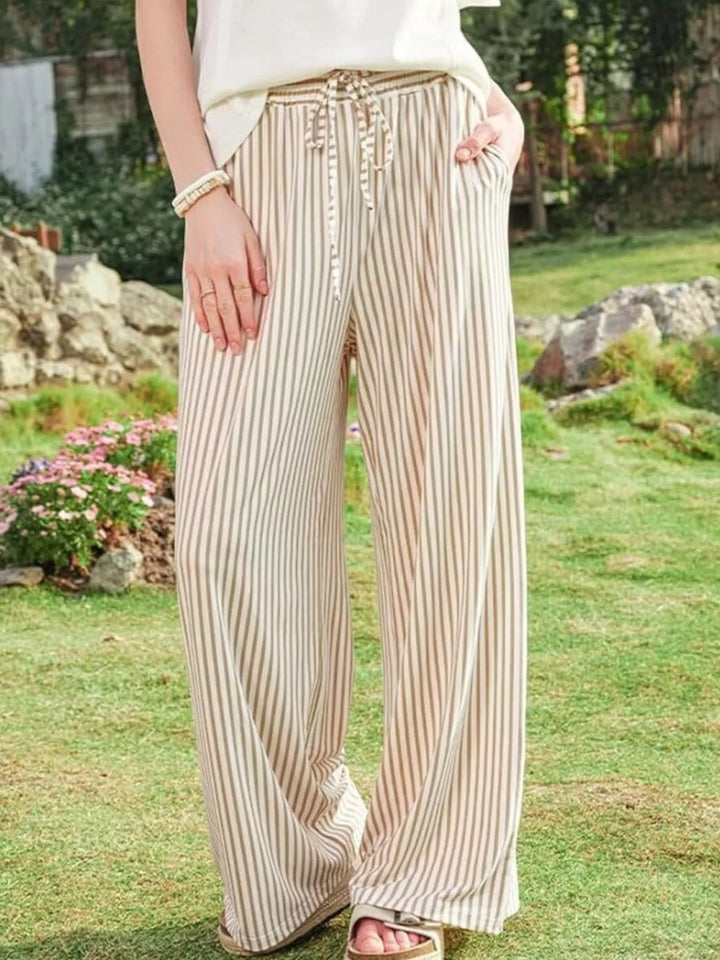 Beige striped wide leg pants with drawstring waist, hand in pocket on the lawn