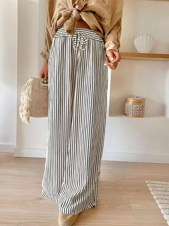 Gray thin stripe wide leg pants with tied tan shirt and woven bag