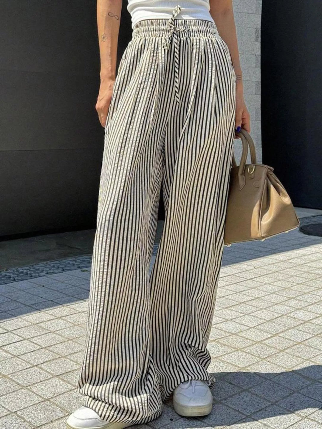 Gray vertical pinstripe wide leg pants with a tan handbag, front view