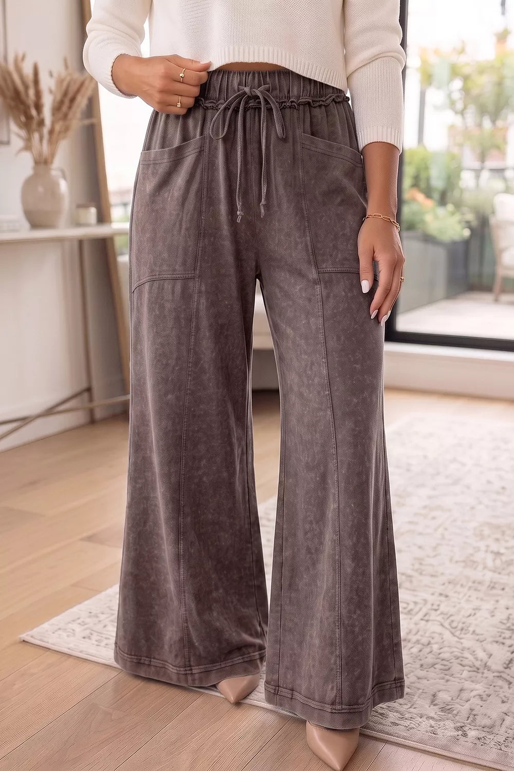 Coffee brown washed pants with patch pockets and a cream top, standing indoors
