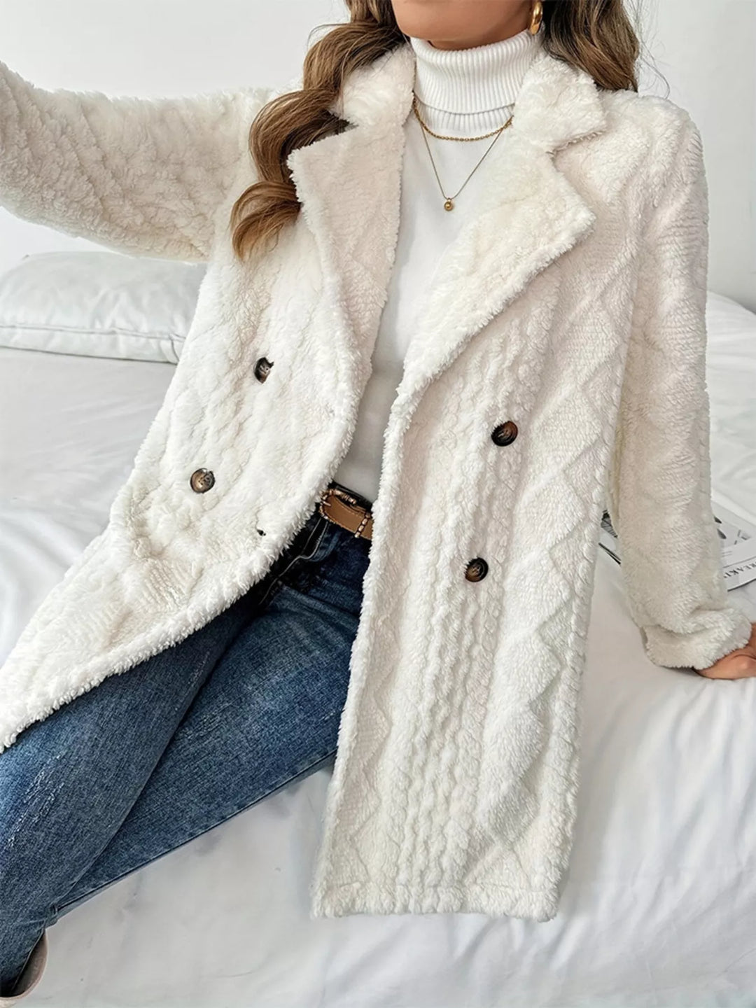 Women's winter coat in ivory, double breasted longline diamond quilt style, seated on a bed
