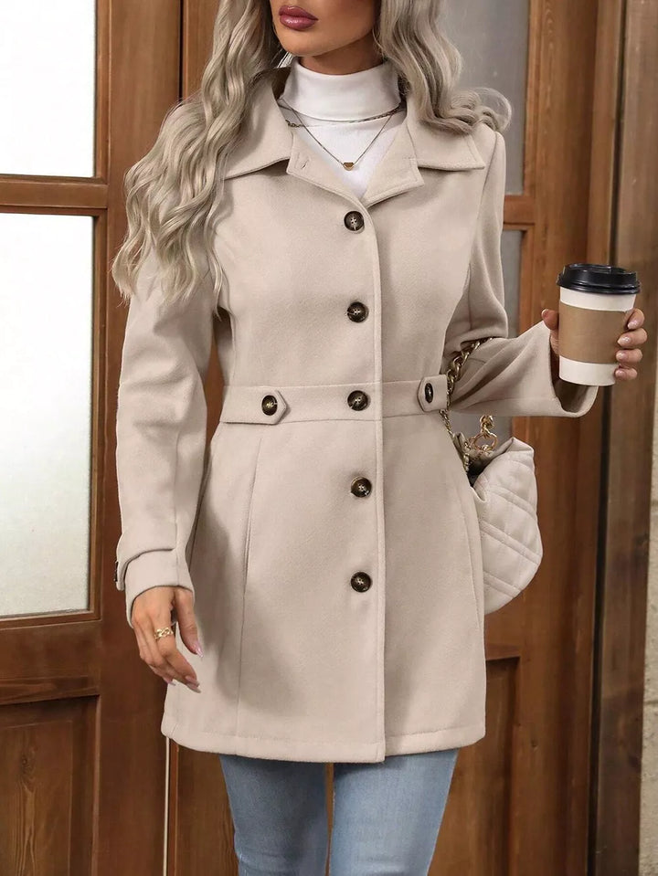 Beige button up winter coat held with a coffee cup, showing the belted waist