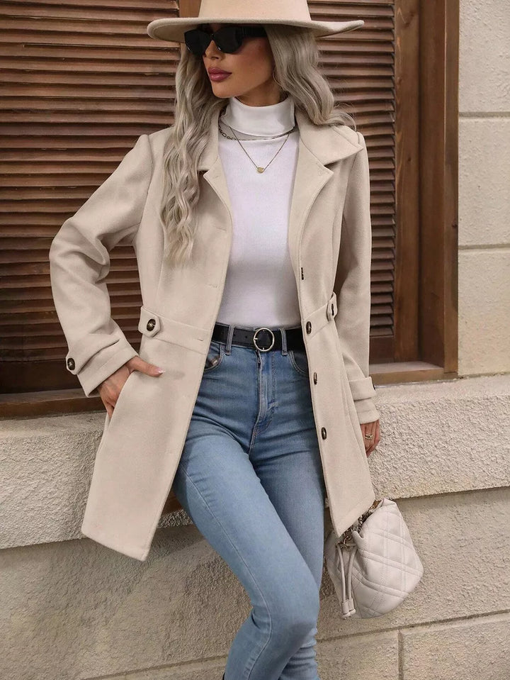 Beige fitted winter coat styled with jeans, a wide brim hat and a white handbag