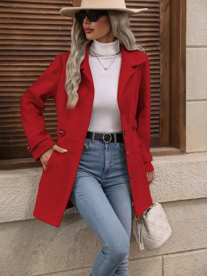 Red winter coat leaning against a wall, styled with a wide brim hat and sunglasses